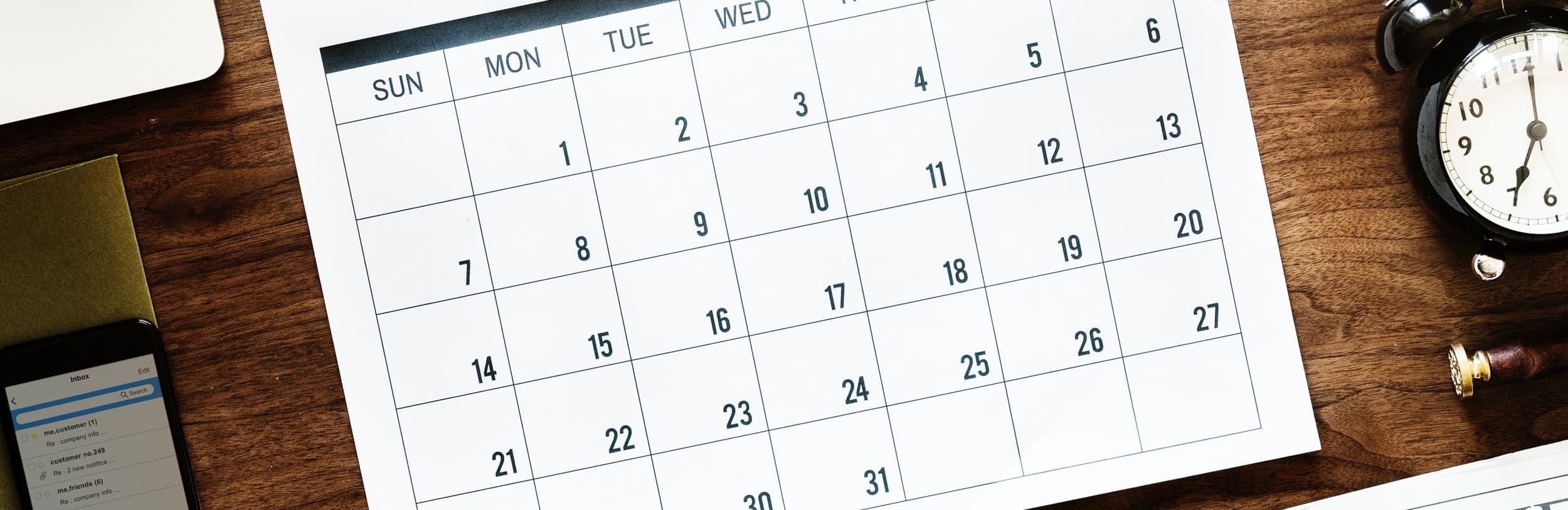 a calendar on a desk next to a phone and clock