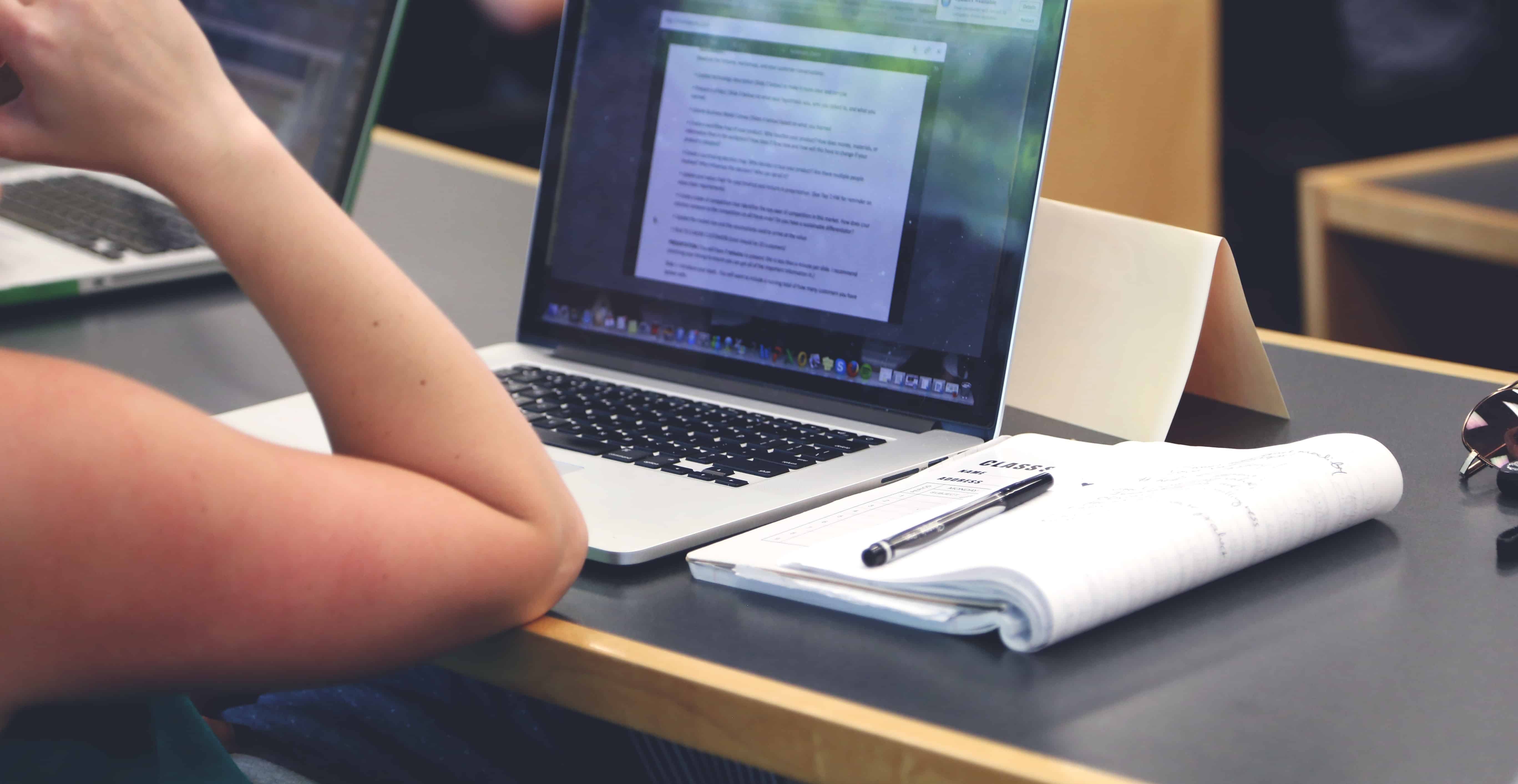 student at a table with laptop, notebook, and pen
