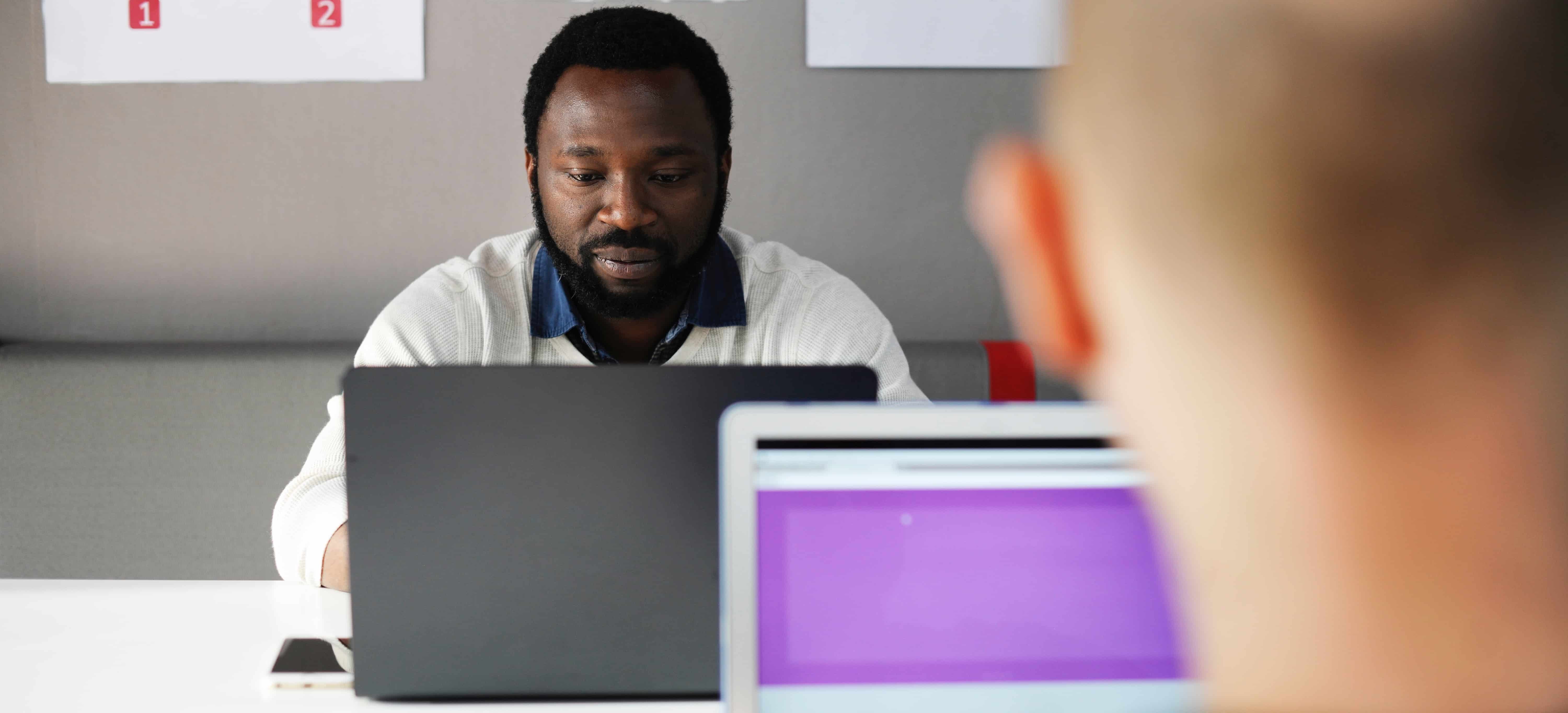 man working at laptop with another man working at laptop out of focus
