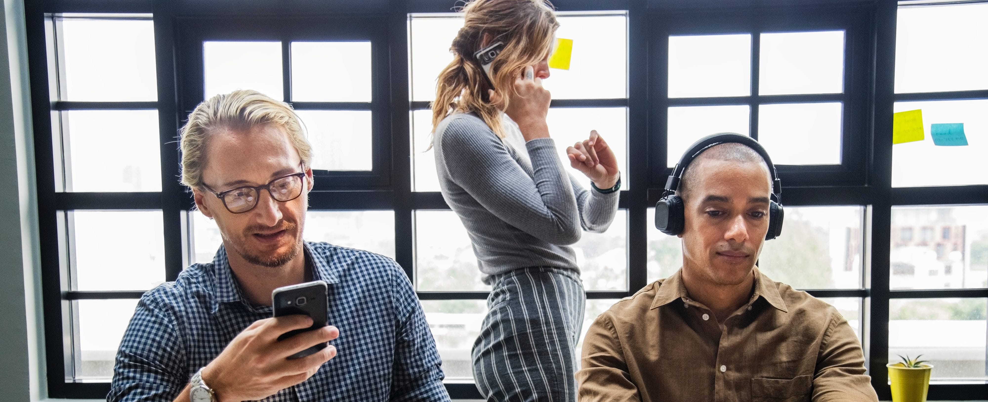 a businessman with glasses checking his phone, a businesswoman speaking on the phone and checking her watch, and a businessman listening to headphones