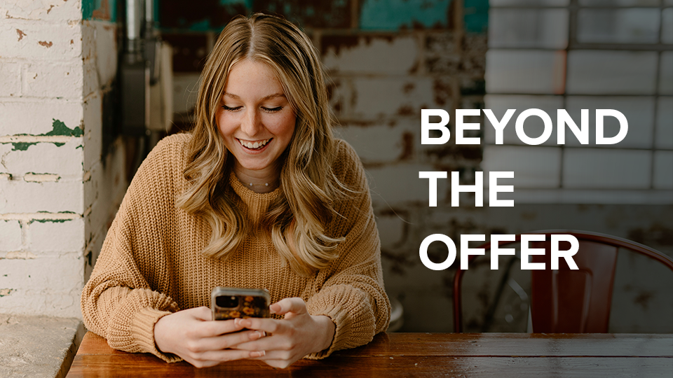 Beyond The Offer - Student sitting at table, looking at phone.